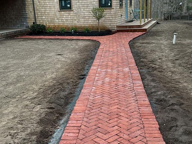 Herringbone brick walkway leading to a shingled cottage