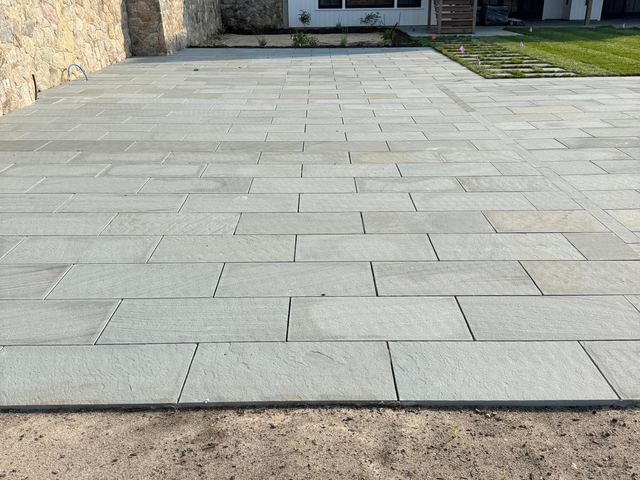 Large bluestone patio behind a house next to a tall stone wall