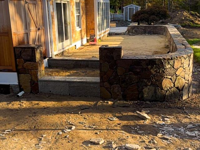 Fieldstone wall around a raised area beside a house